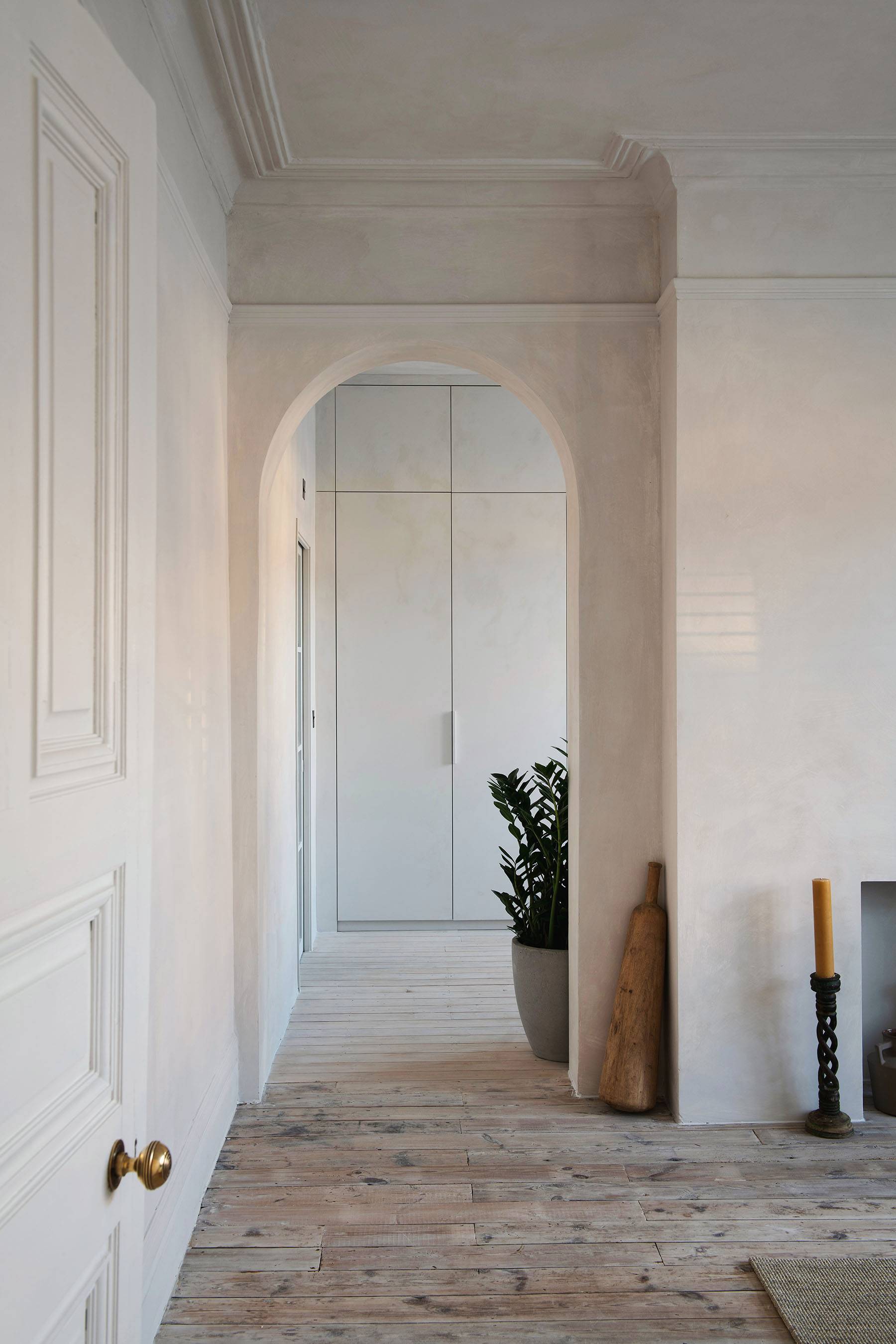 Textured micro-cement hallway passage with arched doorway framing and light wood flooring, Love Locations.