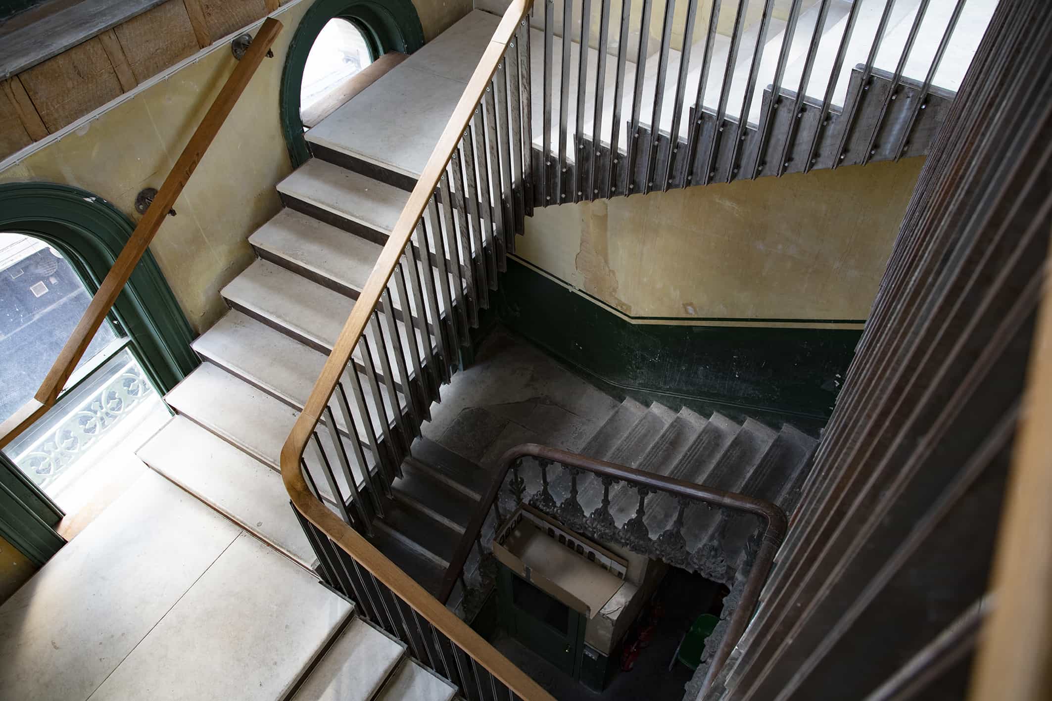 Victorian staircase inside The Old Waiting Room at Peckham Rye, featuring green trim, exposed brick doorways, and raw textured walls.