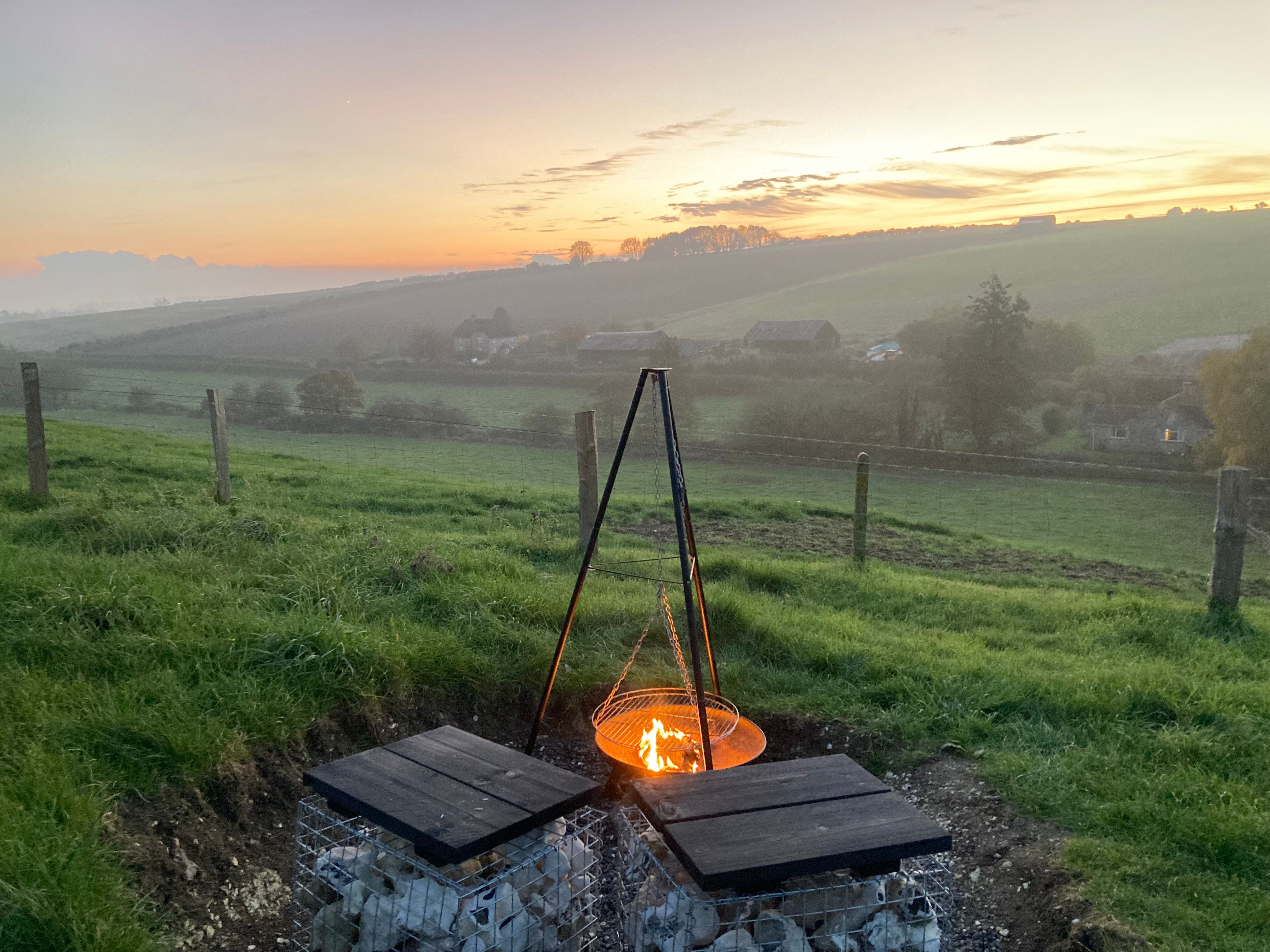 Caption: Outdoor cooking at Bide Cabin, Dorset. A peaceful fire pit area overlooking the fields – perfect for slow meals and golden-hour shoots.