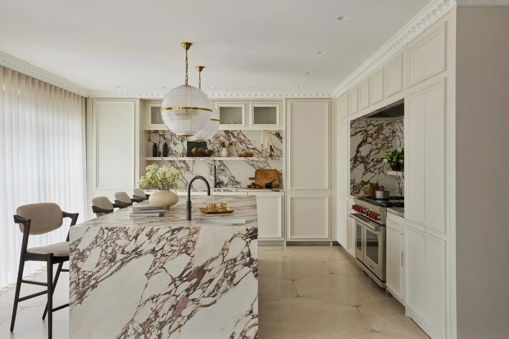 Luxury marble kitchen with a large waterfall island, veined stone surfaces, integrated appliances, brass pendant lighting, and sleek white cabinetry at Linques location.