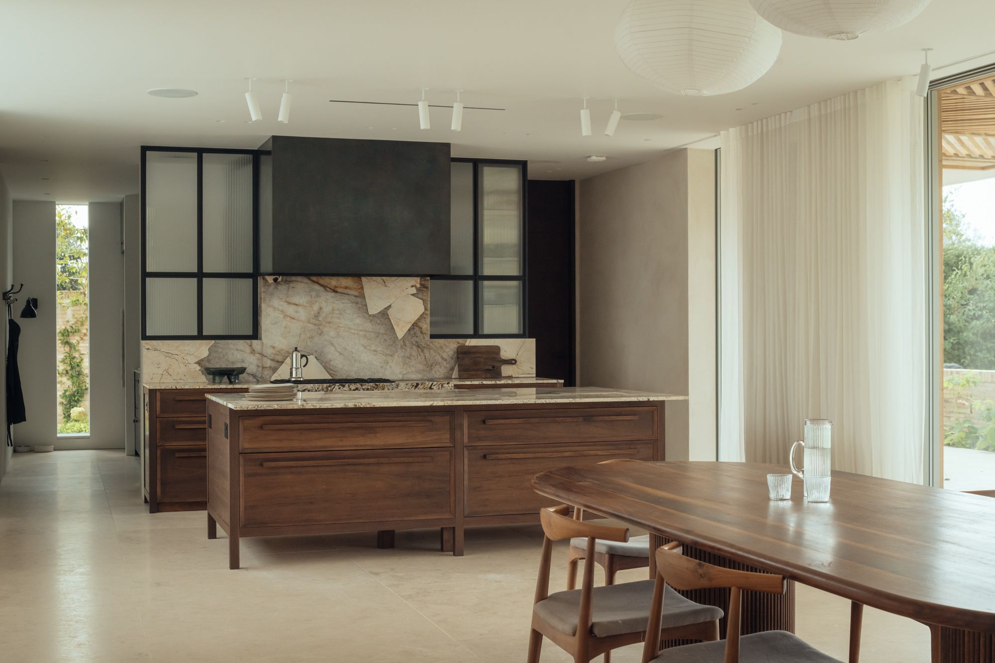 Modern neutral high-end kitcen interior featuring kitcen island, natural wood finishes, marble surfaces, stone elements, and black Crittall-style windows.