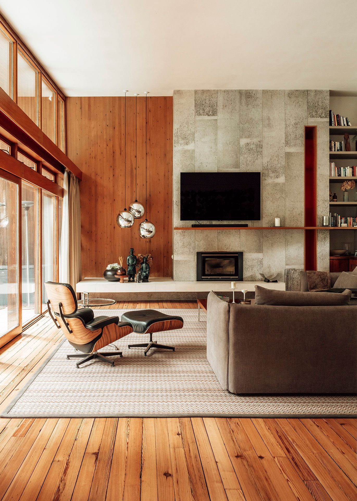 Midcentury interior with high wooden ceilings, retro-style furniture, large sliding doors, silver ball pendant lights, and a stone fireplace with a mounted TV.