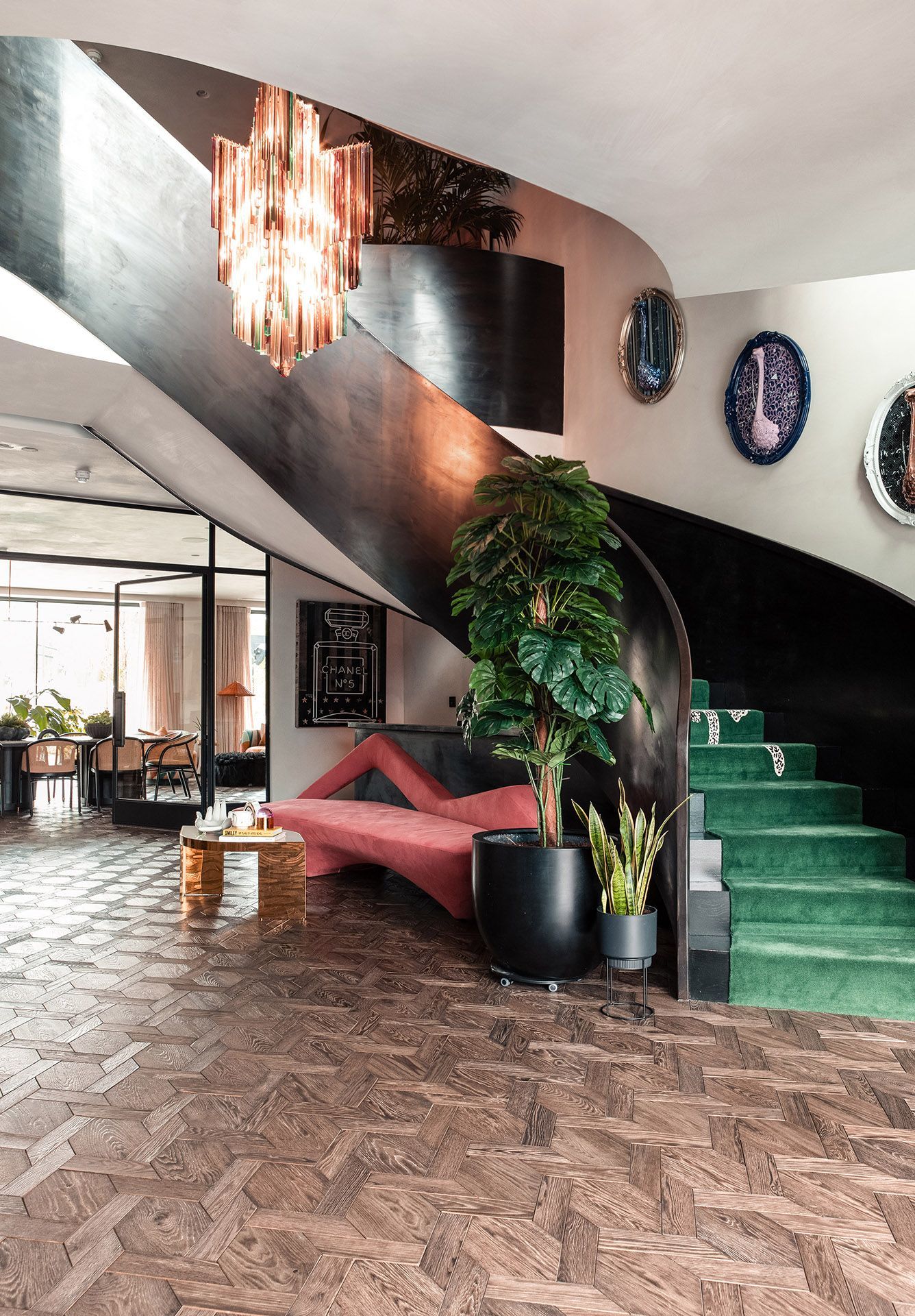 “Radlette – Love Locations. Stunning contemporary hallway featuring a brushed metal curved staircase with green carpet, luxury finishes, wooden parquet flooring, black crittall-style internal doors, and modern oval artworks on the wall.
