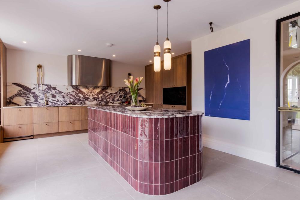location house Chesham with a statement kitchen island tiled in oxeblood tone tiles. Marble splash backs light wood kitchen .