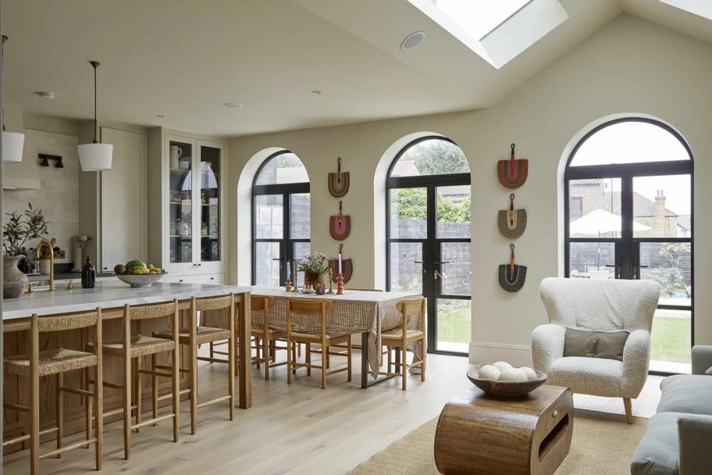 Light-filled kitchen and dining space with arched black-framed windows, natural wood furniture, woven chairs, and soft neutral interiors at Aylward location in SE23.