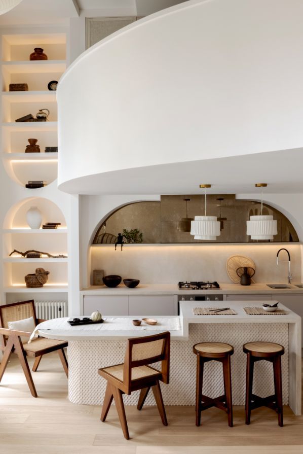 Luxe – Love Locations. Organic sculptured kitchen area with a neutral plaster finish, off-white shelving, and a stylish kitchen island area.