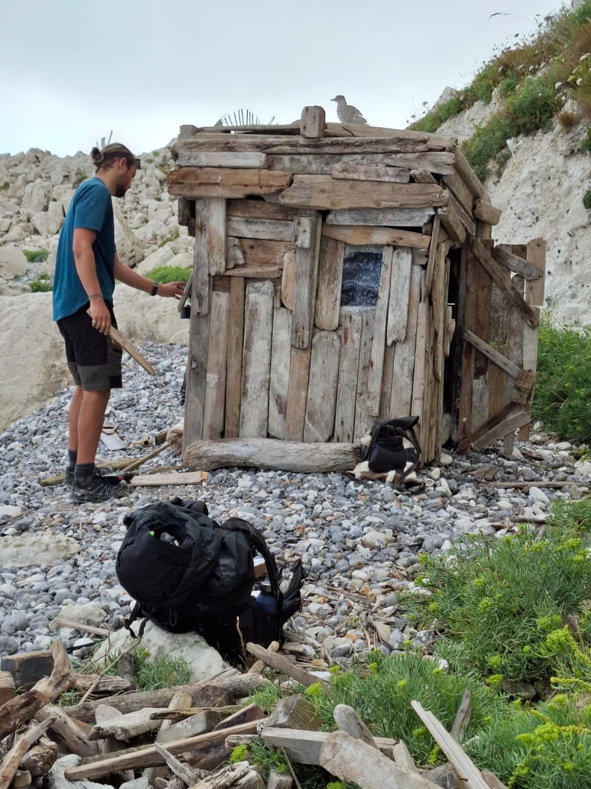 Boy building a small reclaimed wood cabin on a Sussex beach using driftwood – symbolic of creativity and coastal craftsmanship.