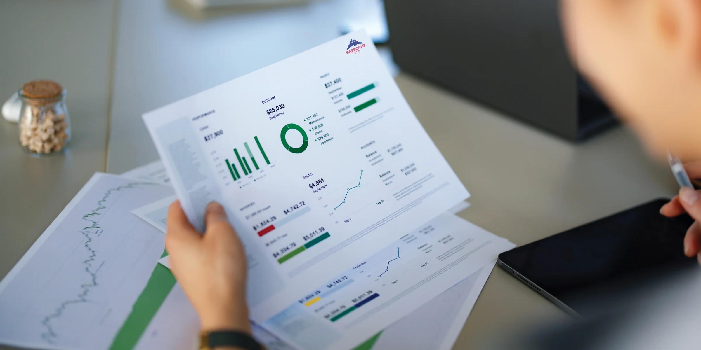 Person reviewing printed business reports with charts, graphs, and performance data at a desk.