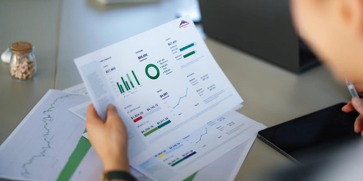 Person reviewing printed business reports with charts, graphs, and performance data at a desk.