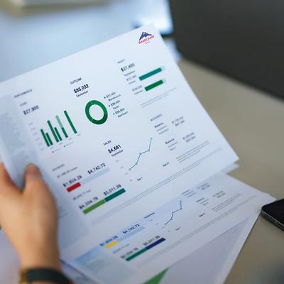 Person reviewing printed business reports with charts, graphs, and performance data at a desk.