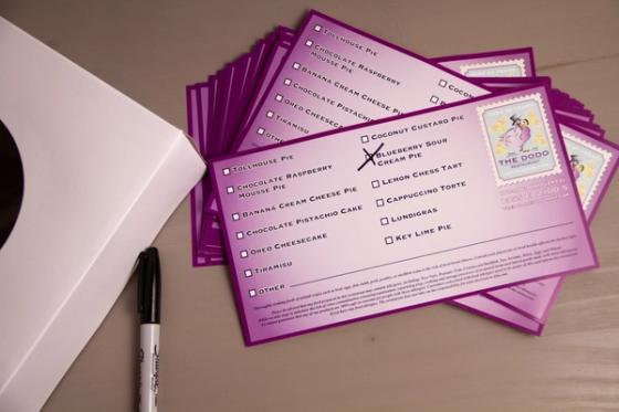 Stack of purple Dodo dessert labels fanned across a table beside a white bakery box and a marker.