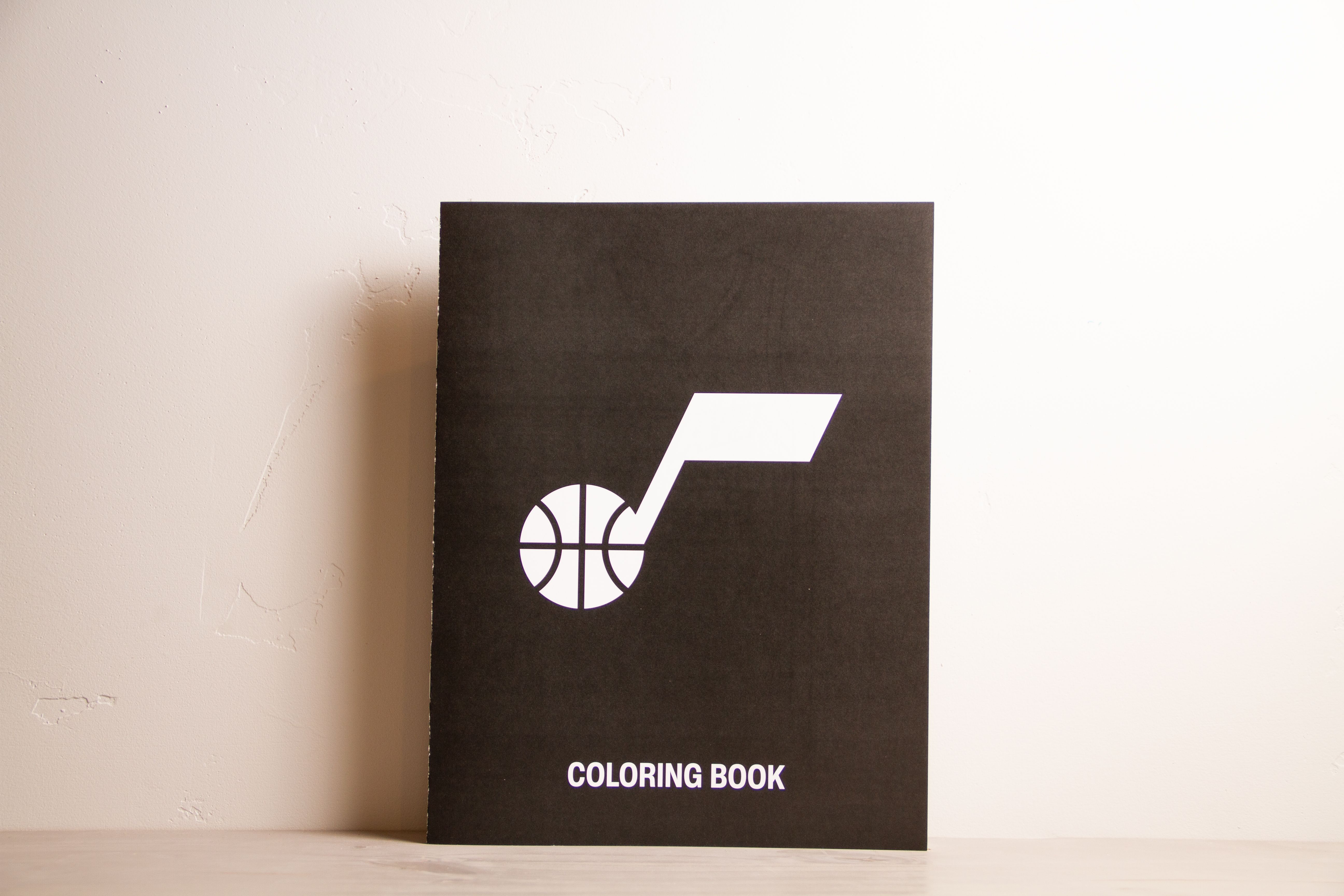 Utah Jazz coloring book standing upright, black cover with the white note-and-basketball logo and the words "Coloring Book."