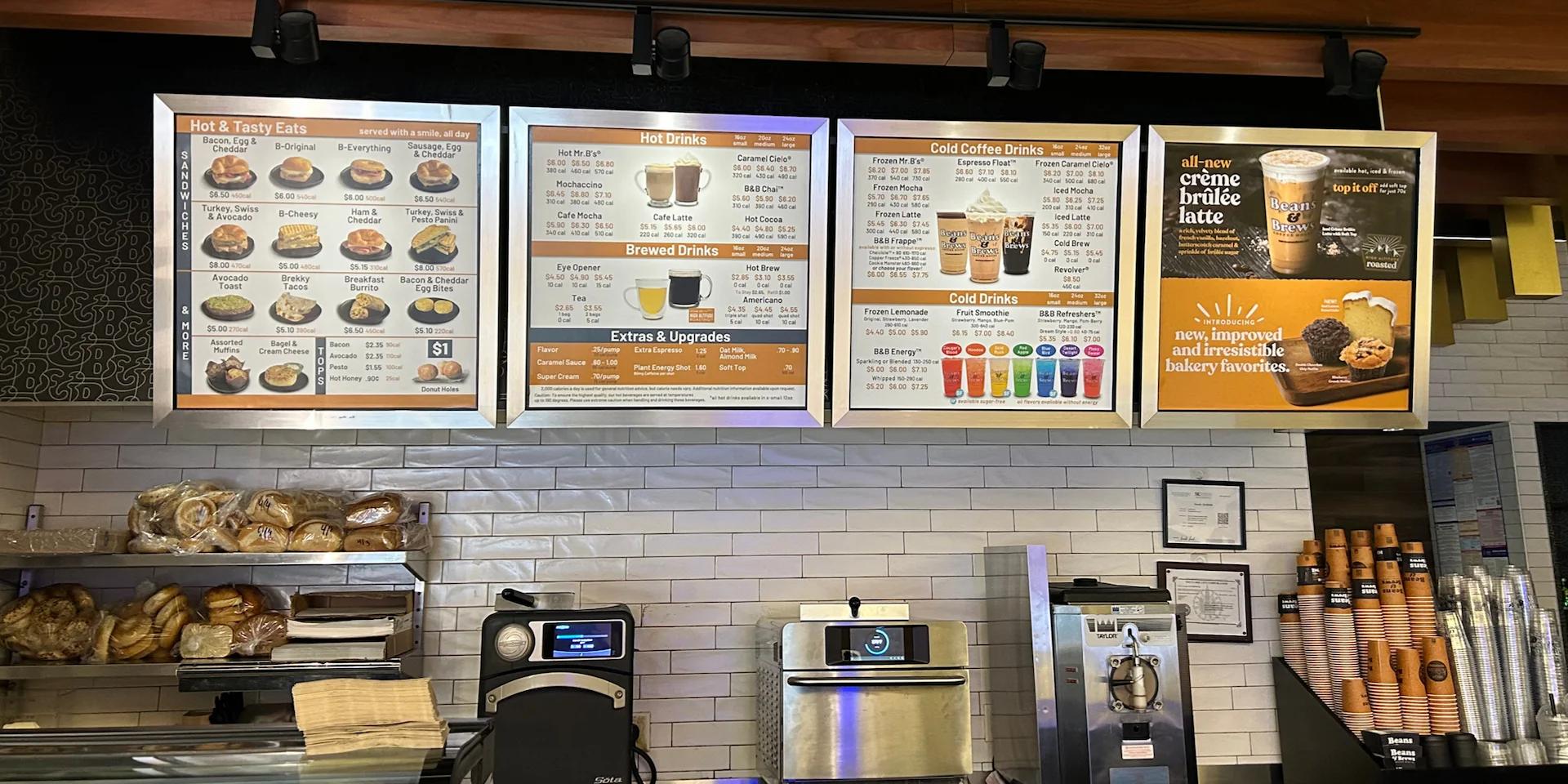 Illuminated café menu boards displaying food and beverage offerings above a service counter.
