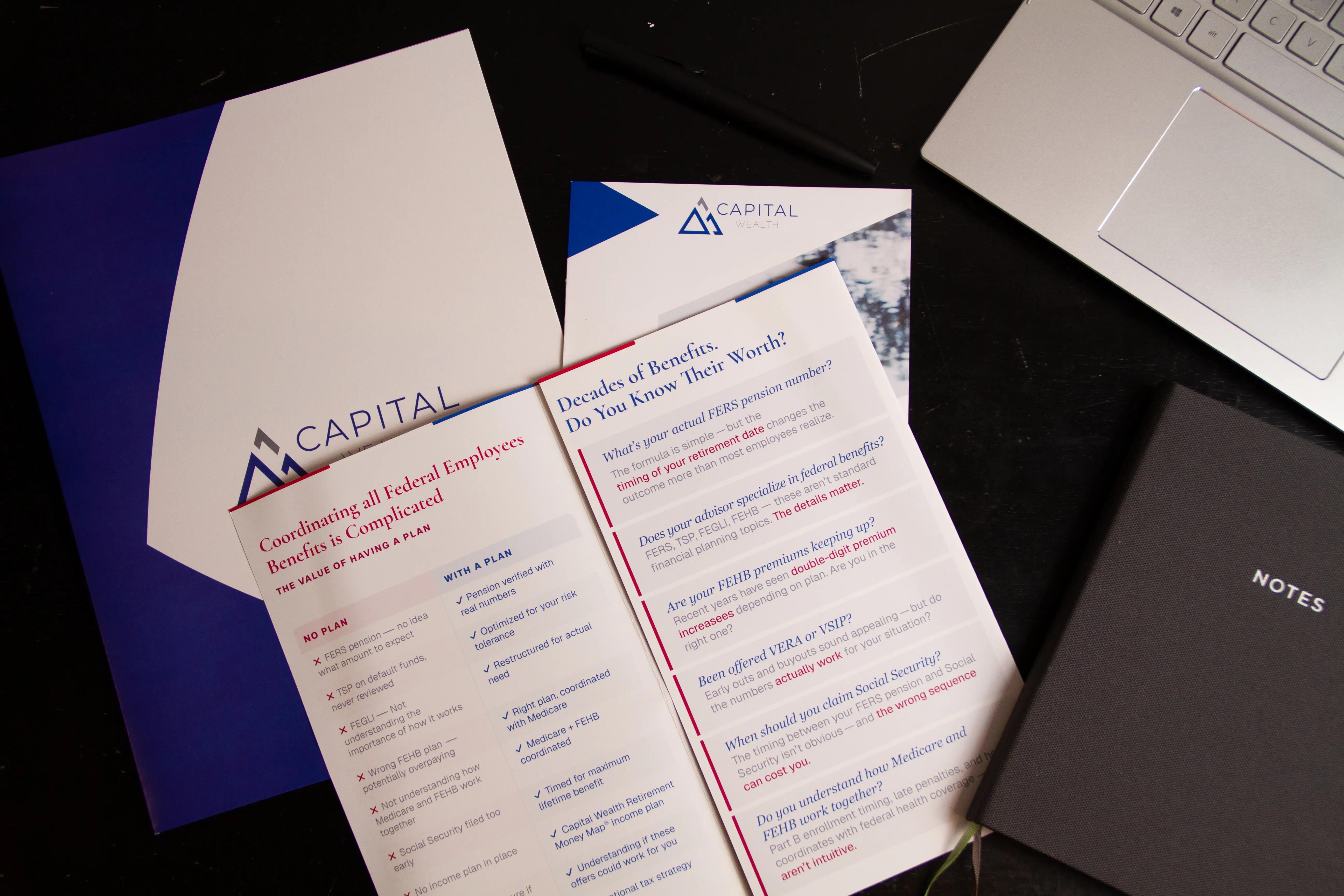 Printed brochures, presentation folders, and business stationery arranged on a desk next to a laptop.