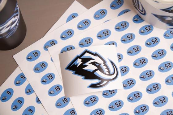 Close overhead view of number label sheets for 9, 19 and 52 with a square Utah Mammoth logo decal laid across them.