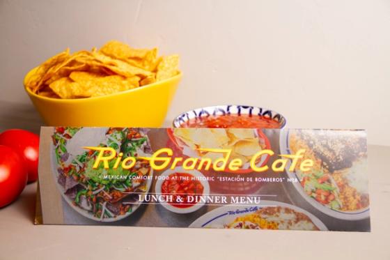 Folded Rio Grande Cafe mailer standing beside chips and salsa, reading "Mexican comfort food at the historic Estación de Bomberos No. 8 — Lunch & Dinner Menu."