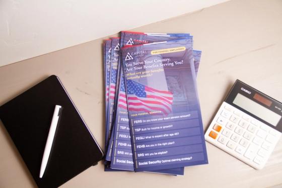 Stack of Capital Wealth federal benefits brochures fanned on a desk beside a black notebook, pen and calculator.