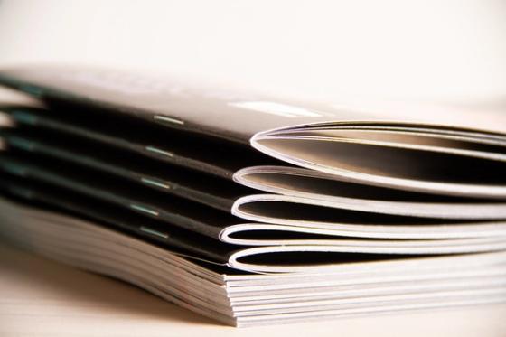 Close-up of the folded spines of stacked booklets, showing two staples per spine and white interior page edges against black covers.