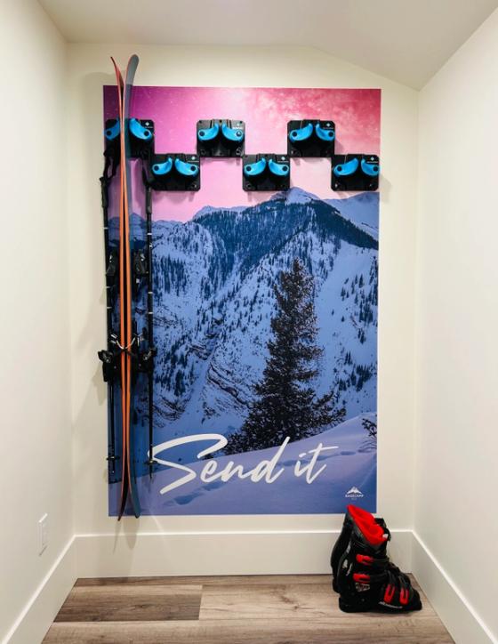 Floor-to-ceiling alpine graphic reading "Send it" with the Basecamp SLC logo, fitted with ski racks holding skis and poles.