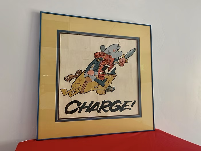 A framed vintage poster of a red-bearded cartoon general in a gray hat and blue coat, leaning forward mid-stride with a sword raised, above the word "CHARGE!" in bold black letters.