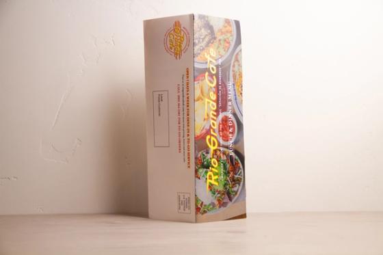 Folded mailer standing on end, showing the narrow finished size with the postal panel and food photography meeting at the fold.