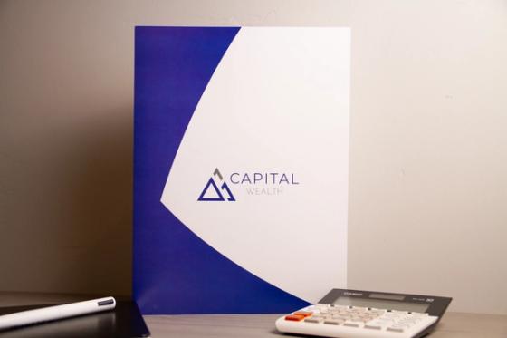 Capital Wealth presentation folder standing upright, blue and white with a curved diagonal split and the mountain triangle logo centered.