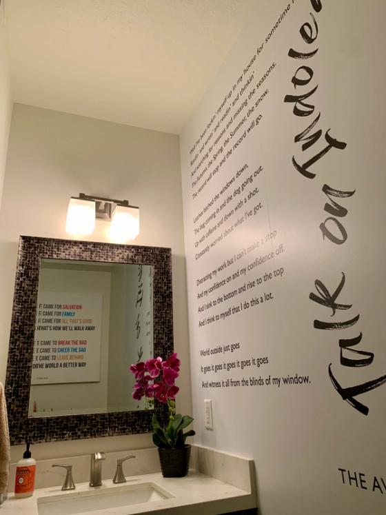 Powder room wall printed with song lyrics in italic and brush lettering, with a matching lyric canvas reflected in the mirror.