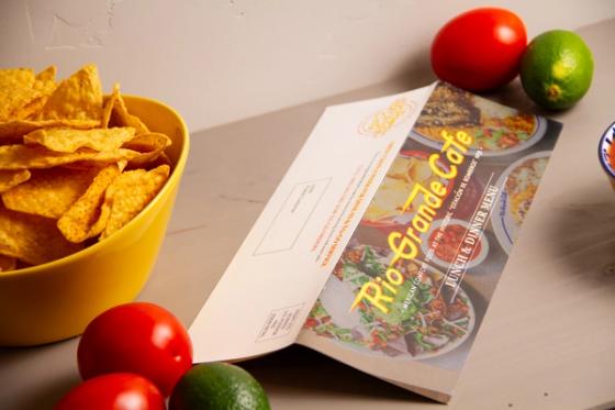 Mailer partly unfolded, showing the printed food panel opening away from the white postal panel.