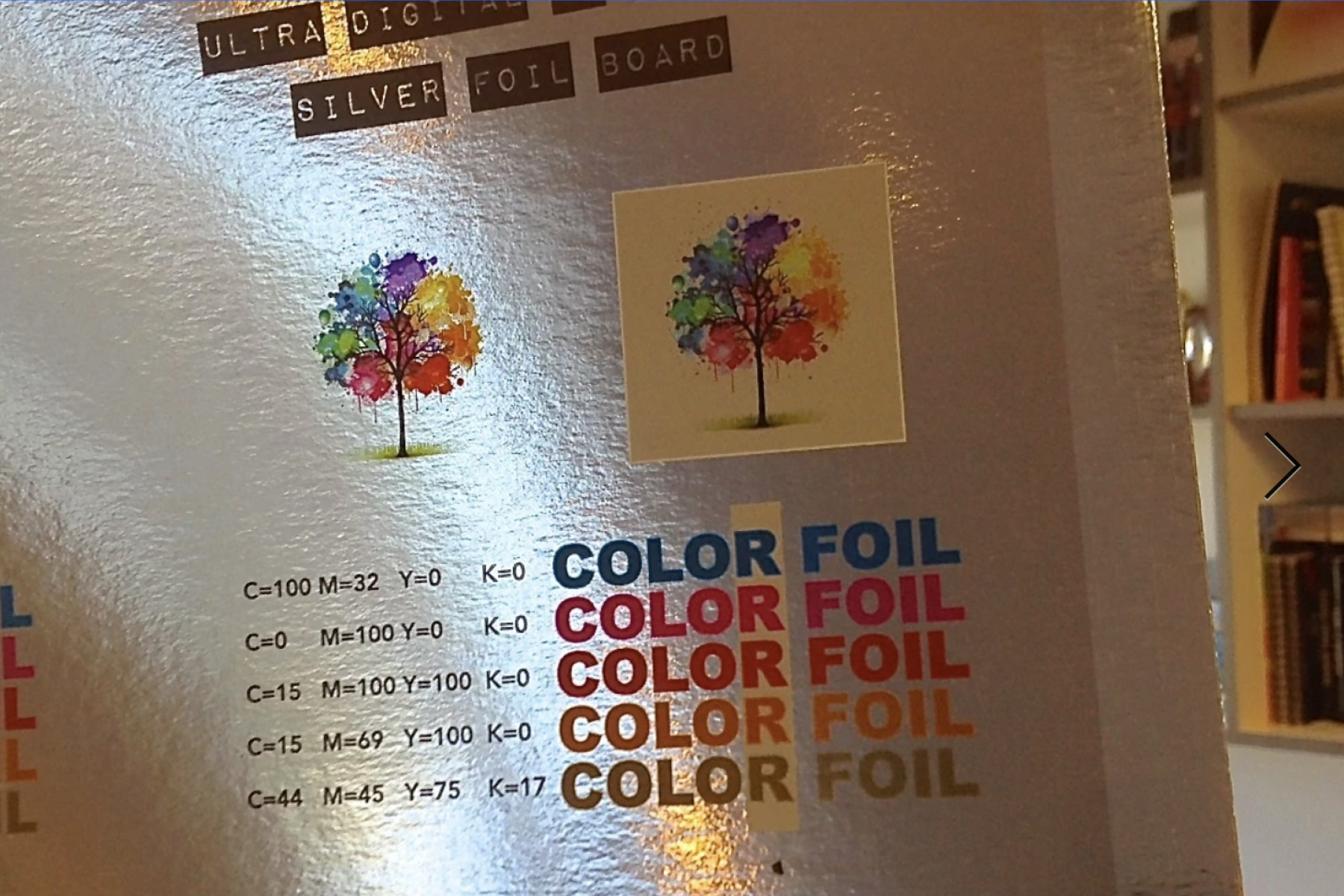 Silver foil printing sample board showing a watercolor tree illustration printed on reflective foil and on a cream background, above a CMYK color chart with 'COLOR FOIL' printed in five colors.