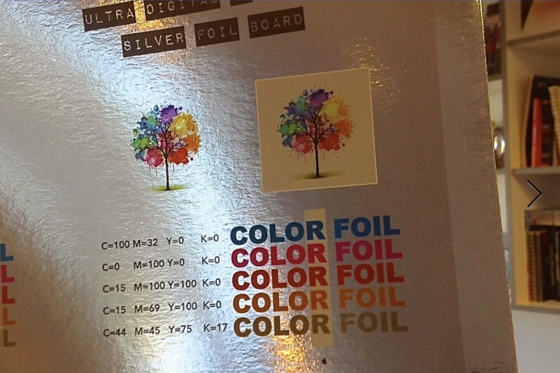Silver foil printing sample board showing a watercolor tree illustration printed on reflective foil and on a cream background, above a CMYK color chart with 'COLOR FOIL' printed in five colors.