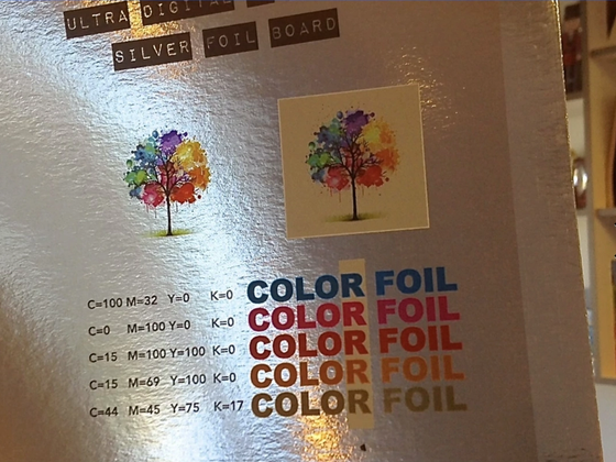 Silver foil printing sample board showing a watercolor tree illustration printed on reflective foil and on a cream background, above a CMYK color chart with 'COLOR FOIL' printed in five colors.