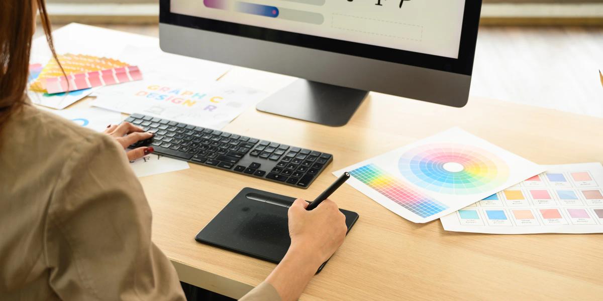 Graphic designer creating a custom print design using professional design software, color swatches, and a drawing tablet.