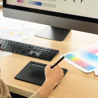 Graphic designer creating a custom print design using professional design software, color swatches, and a drawing tablet.