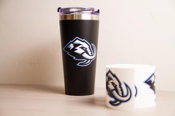 Black insulated tumbler with the Utah Mammoth logo applied, beside a roll of white vinyl printed with the same logo.