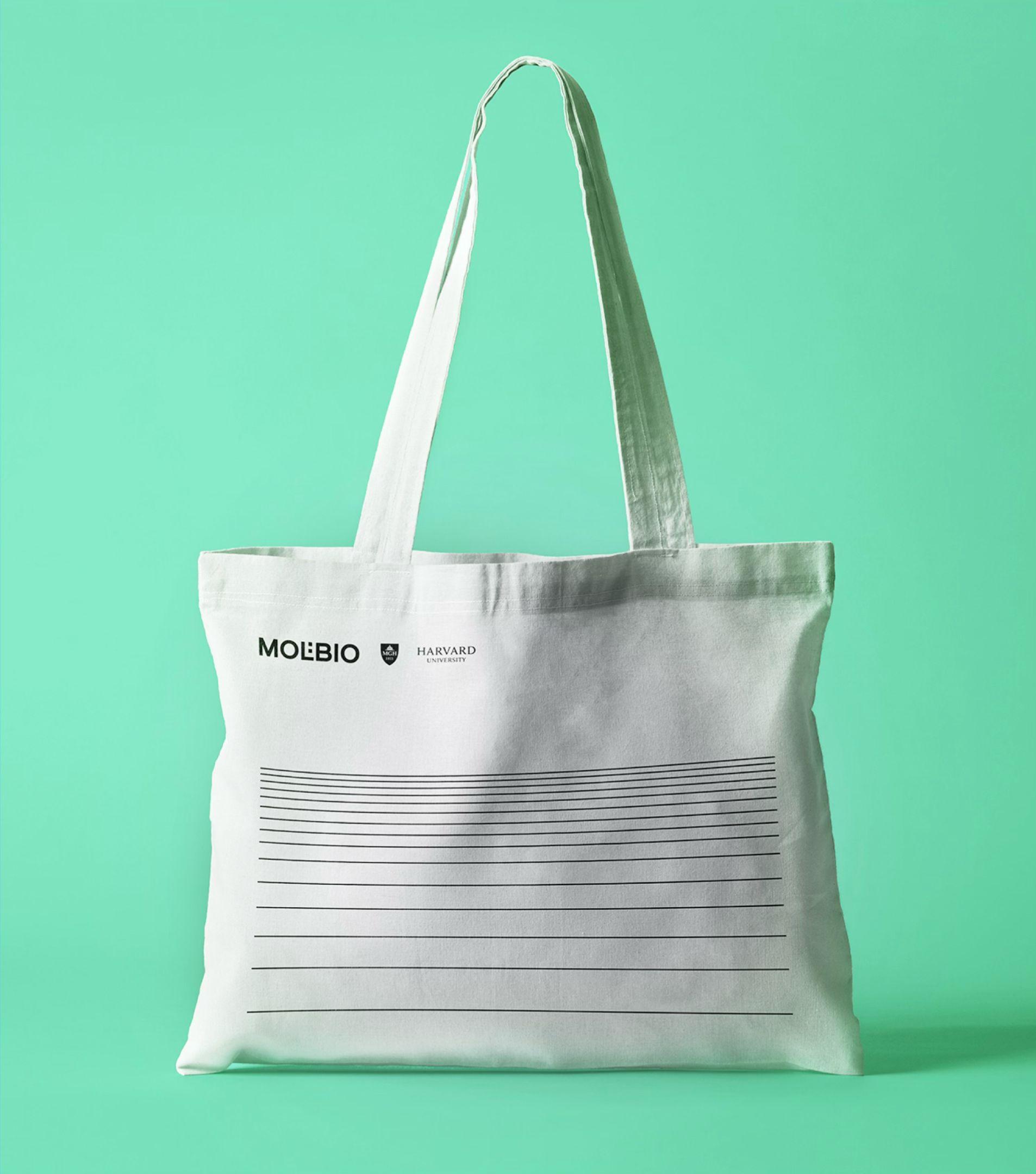 White Molbio tote bag with the Harvard University logo and a band of horizontal lines, on a green background