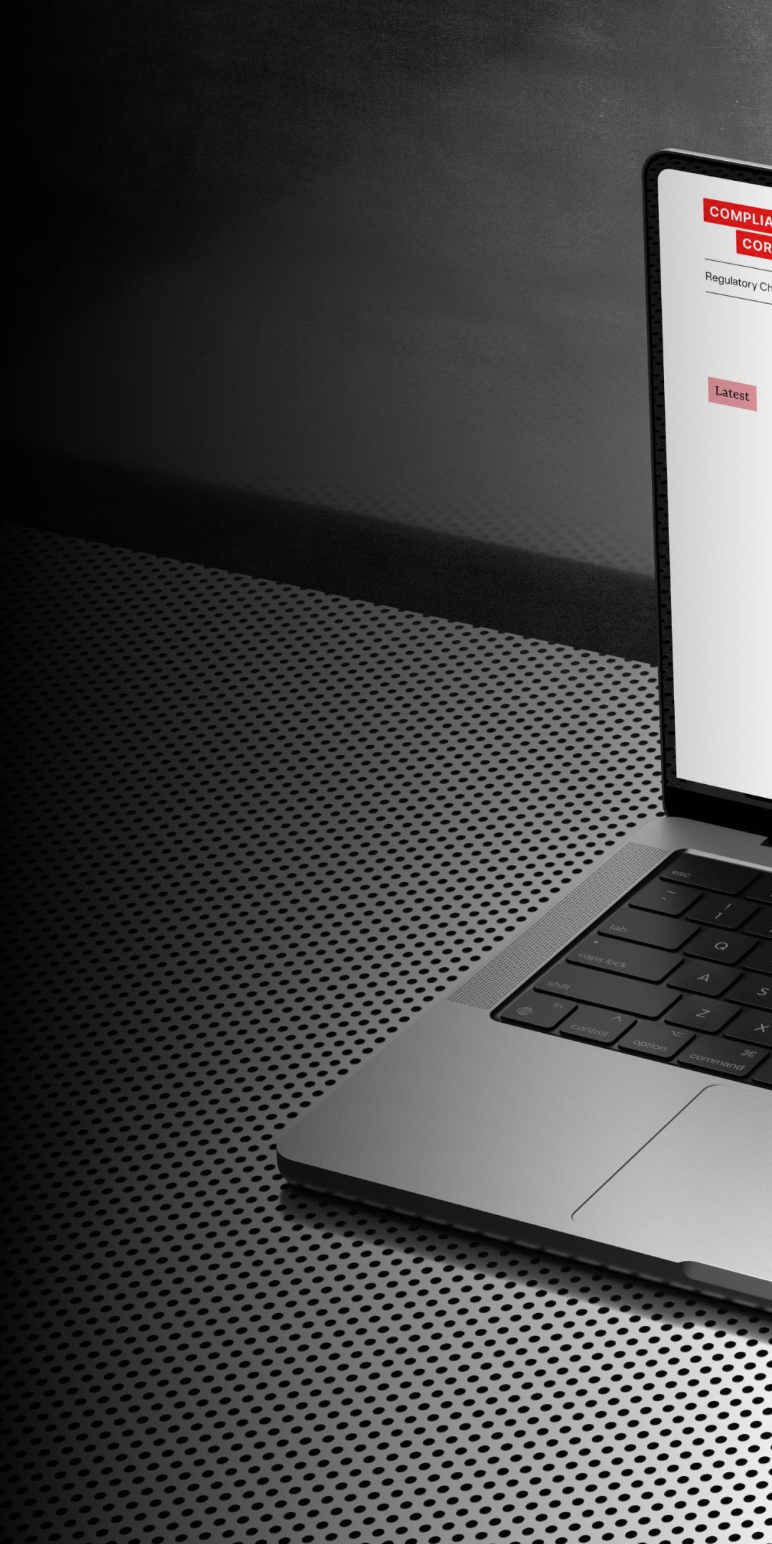 Compliance Corylated news site on a laptop, showing a lead story above a grid of articles