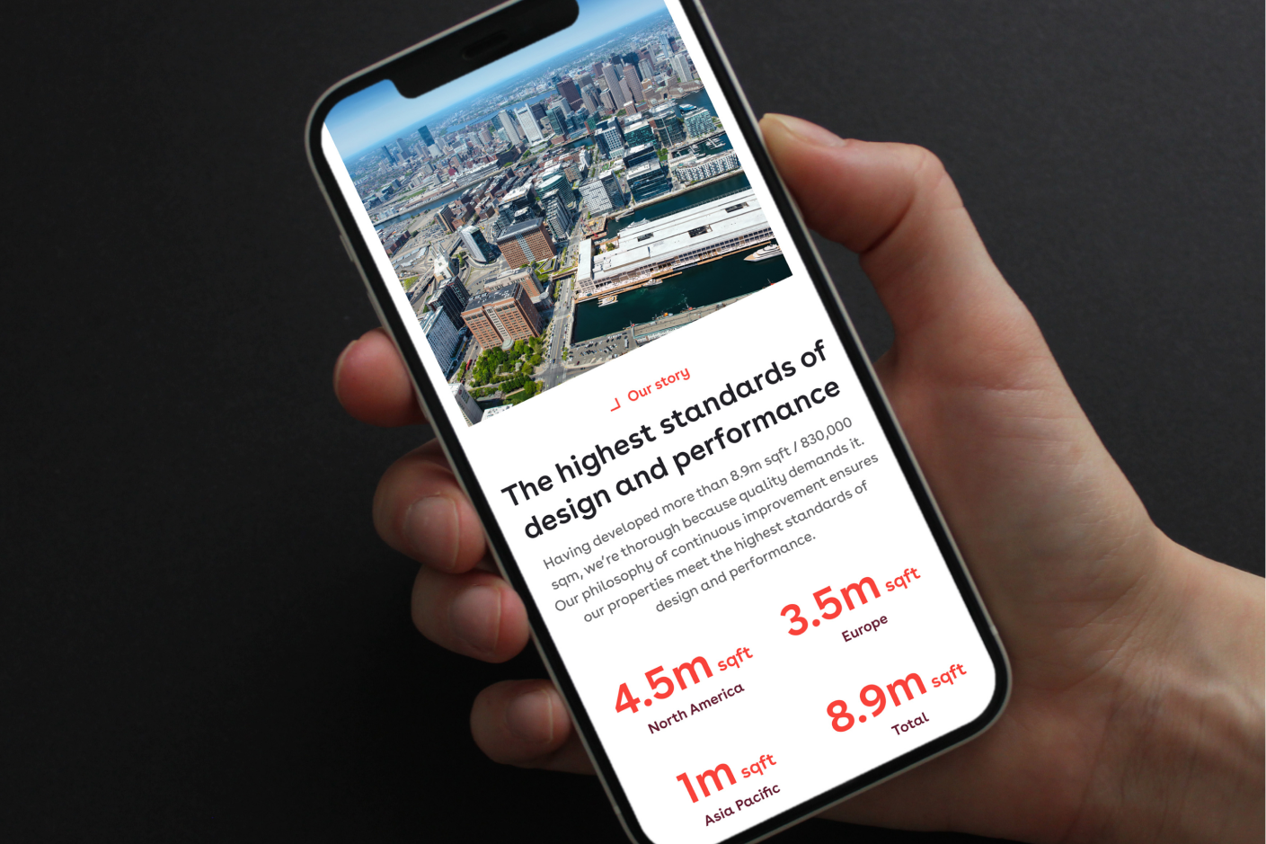 Hand holding a phone showing Pembroke's "Our story" page with 8.9m sq ft developed across North America, Europe and Asia Pacific