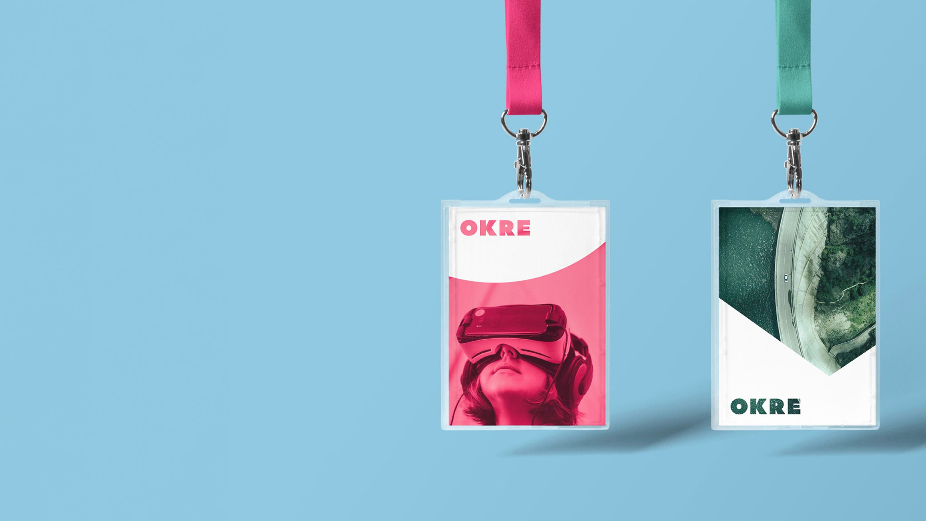 Two OKRE lanyard passes, one pink with a person in a VR headset, one green with an aerial view of a road