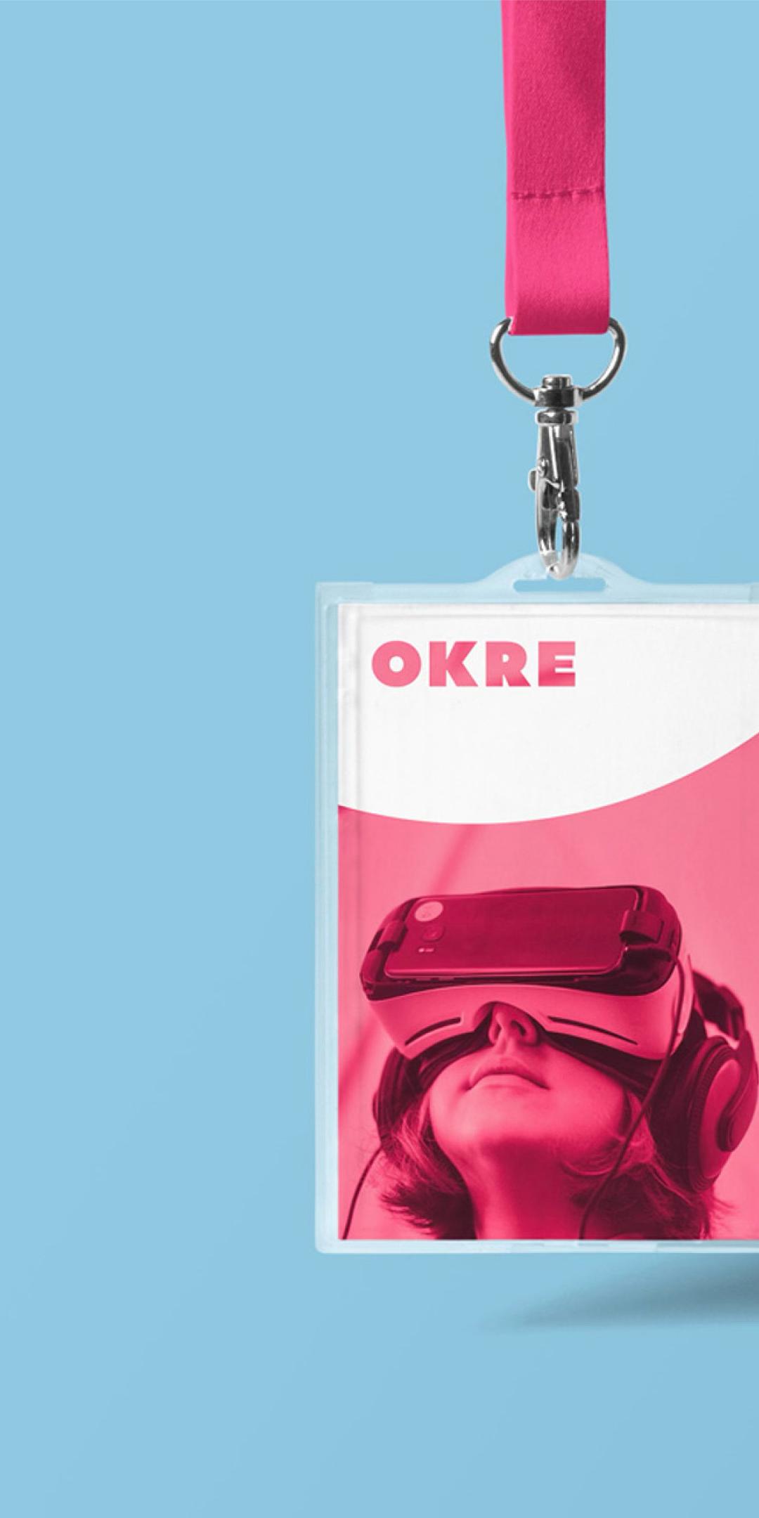 Two OKRE lanyard passes, one pink with a person in a VR headset, one green with an aerial view of a road