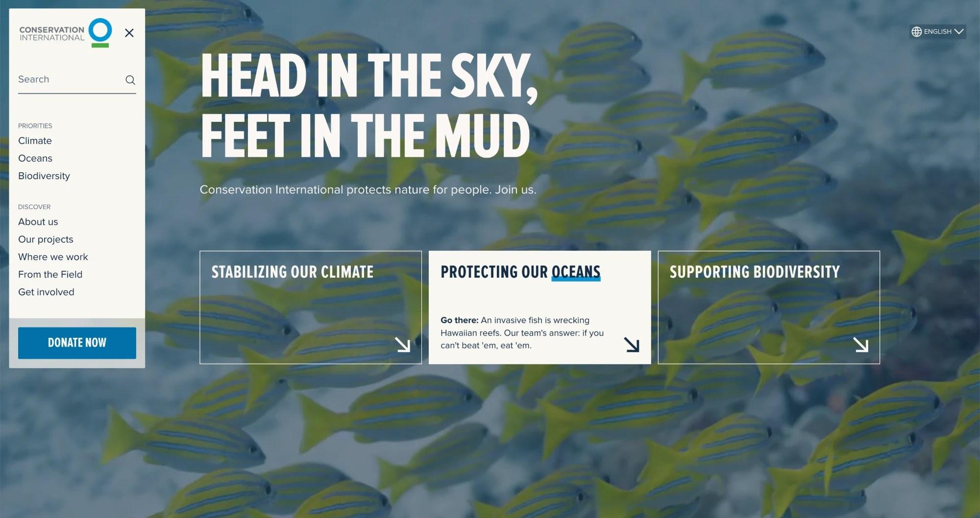 Conservation International's homepage: "Head in the sky, feet in the mud" over a shoal of fish, with the menu open and the three priorities, climate, oceans and biodiversity, as ways in