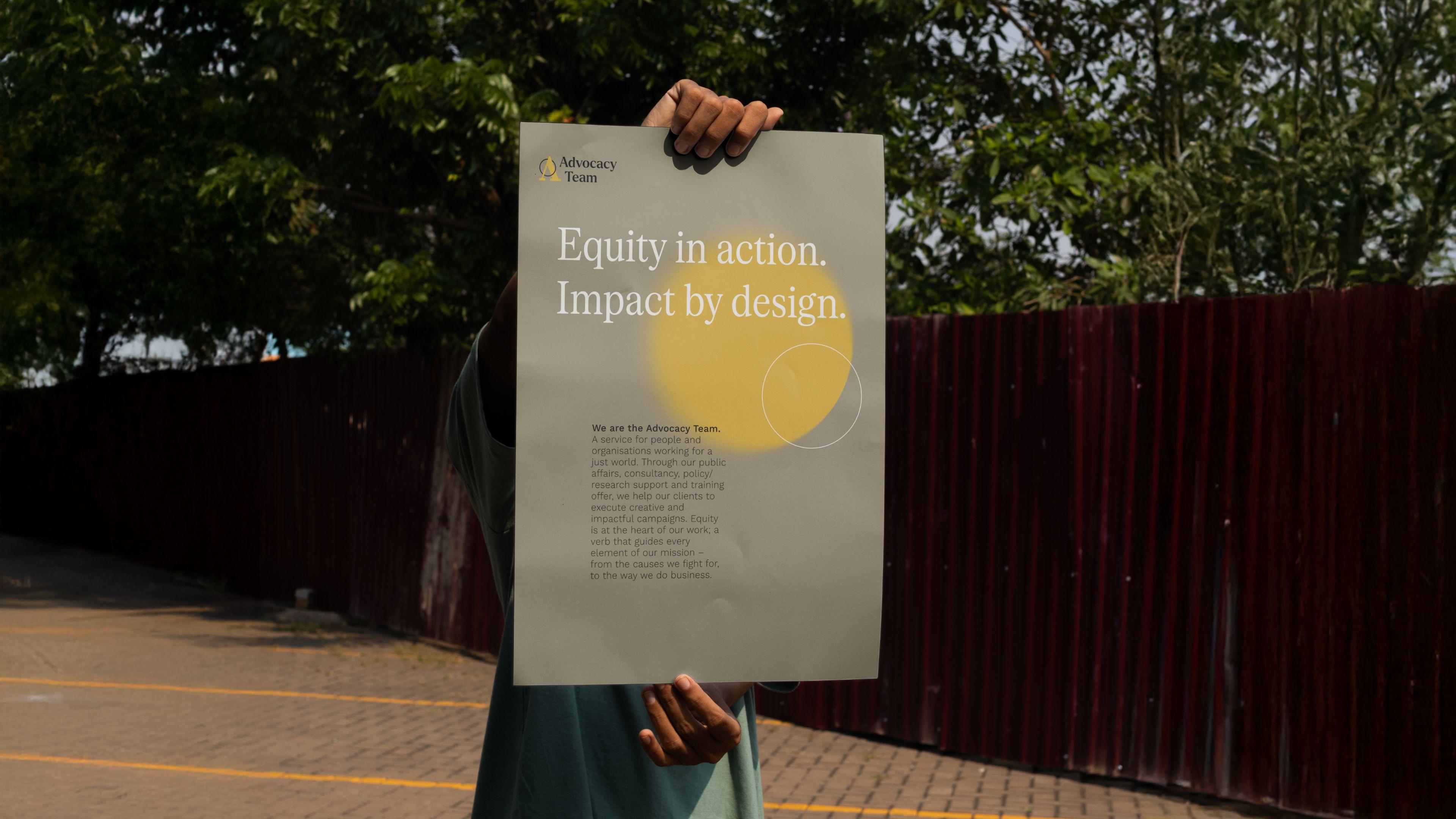 Someone holding up an Advocacy Team poster outdoors that reads "Equity in action. Impact by design."