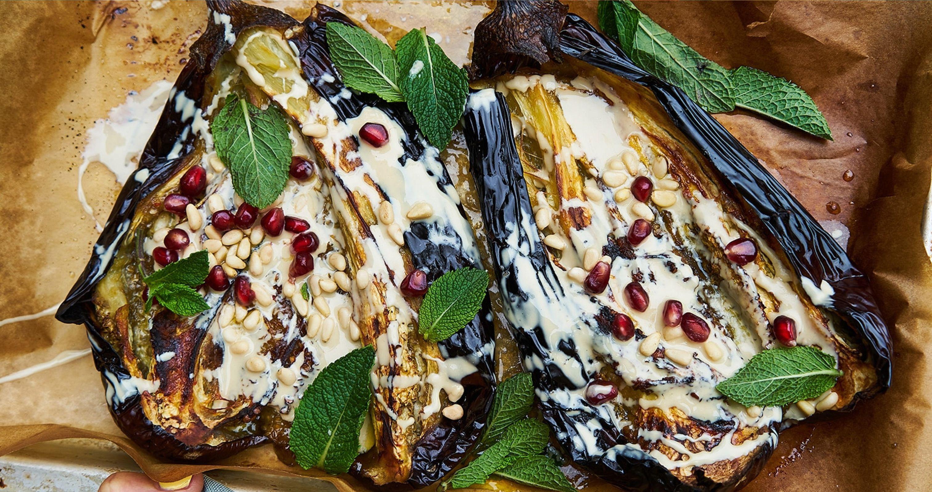 Roasted aubergine halves topped with a creamy dressing, pomegranate seeds, pine nuts and mint leaves