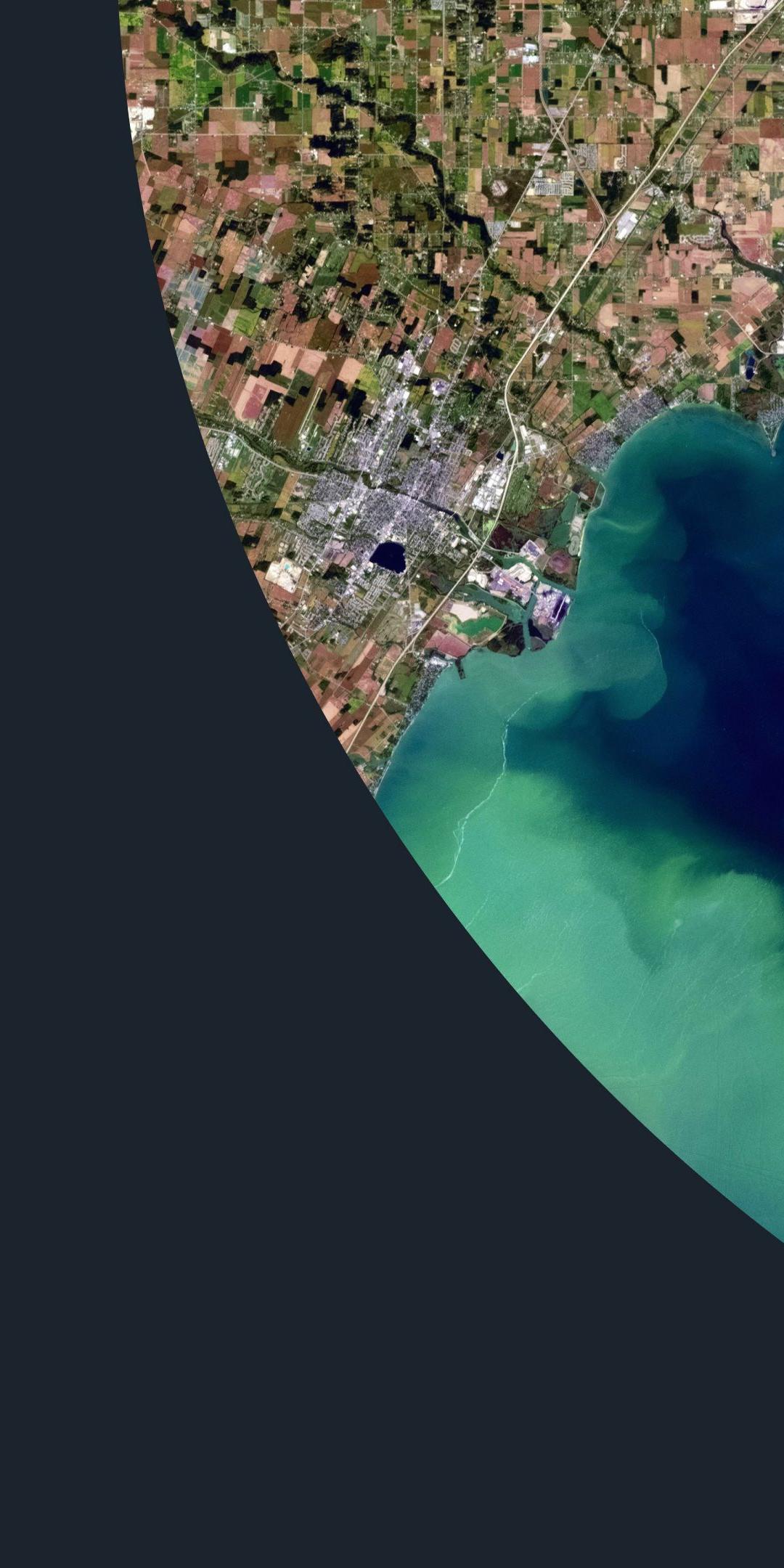 Satellite view of a coastline with green algae swirling through blue water, framed by a large curve