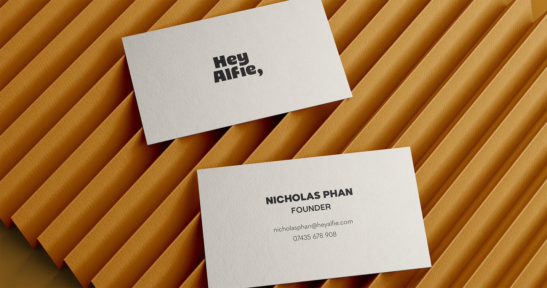 Front and back of Hey Alfie business cards, one with the logo and one with the founder's contact details, on folded orange card