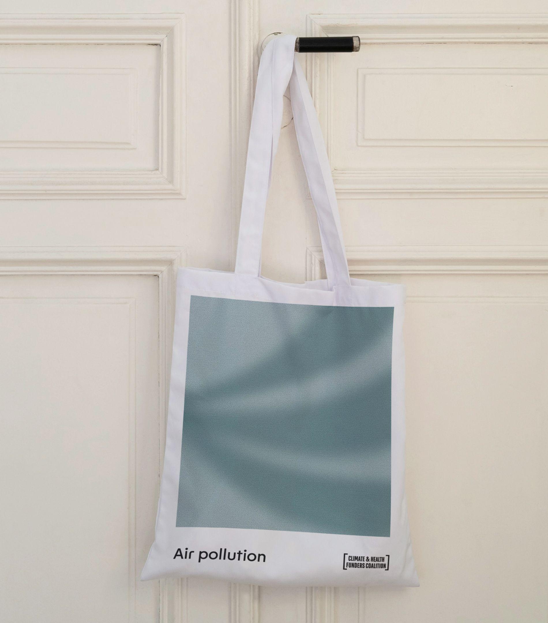 White Climate & Health Funders Coalition tote bag with a blue-green gradient and the label "Air pollution", hung on a door handle
