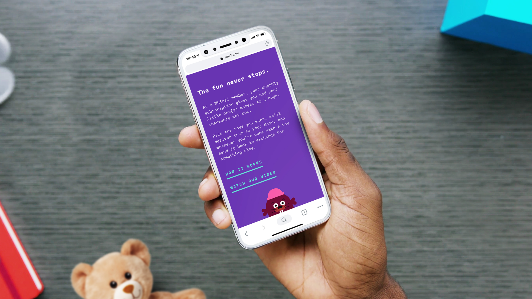 Hand holding a phone showing the Whirli mobile site, "The fun never stops.", with a cartoon character