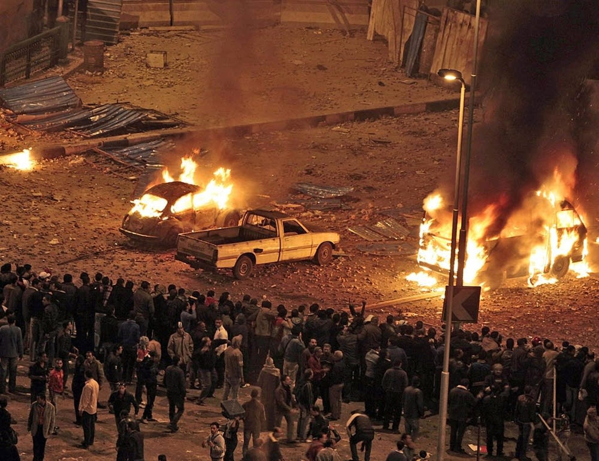 Pro-government demonstrators watch as cars burn during clashes with anti-government demonstrators in Tahrir square