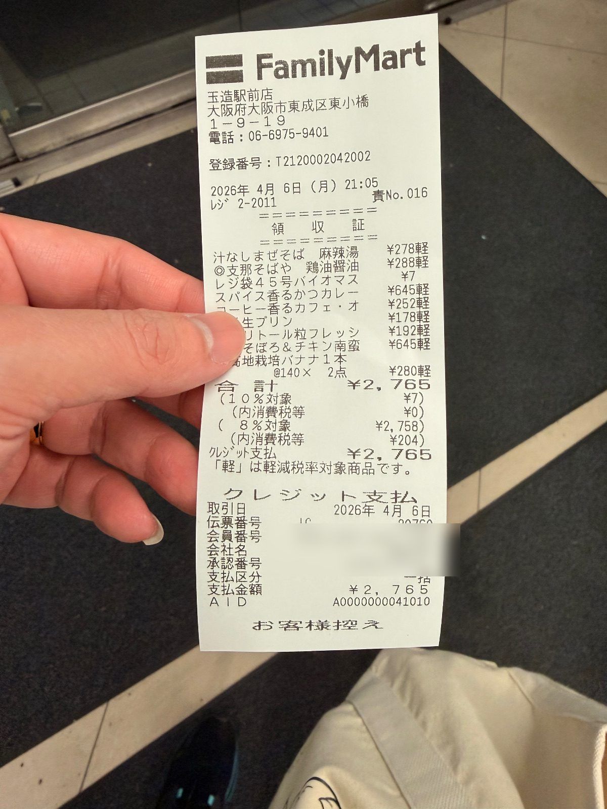 FamilyMart receipt from Tamatsukuri, Osaka, listing ten items including instant noodles, curry and a banana, with a 7 yen bag charge and a 2,765 yen total, card details blurred