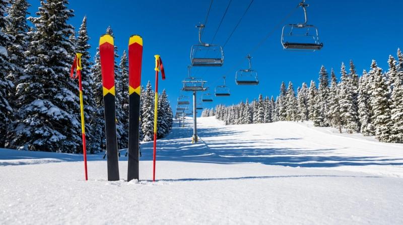 A pair of red and yellow skis and poles planted in fresh powder snow below an empty chairlift, under a clear blue sky at a ski resort