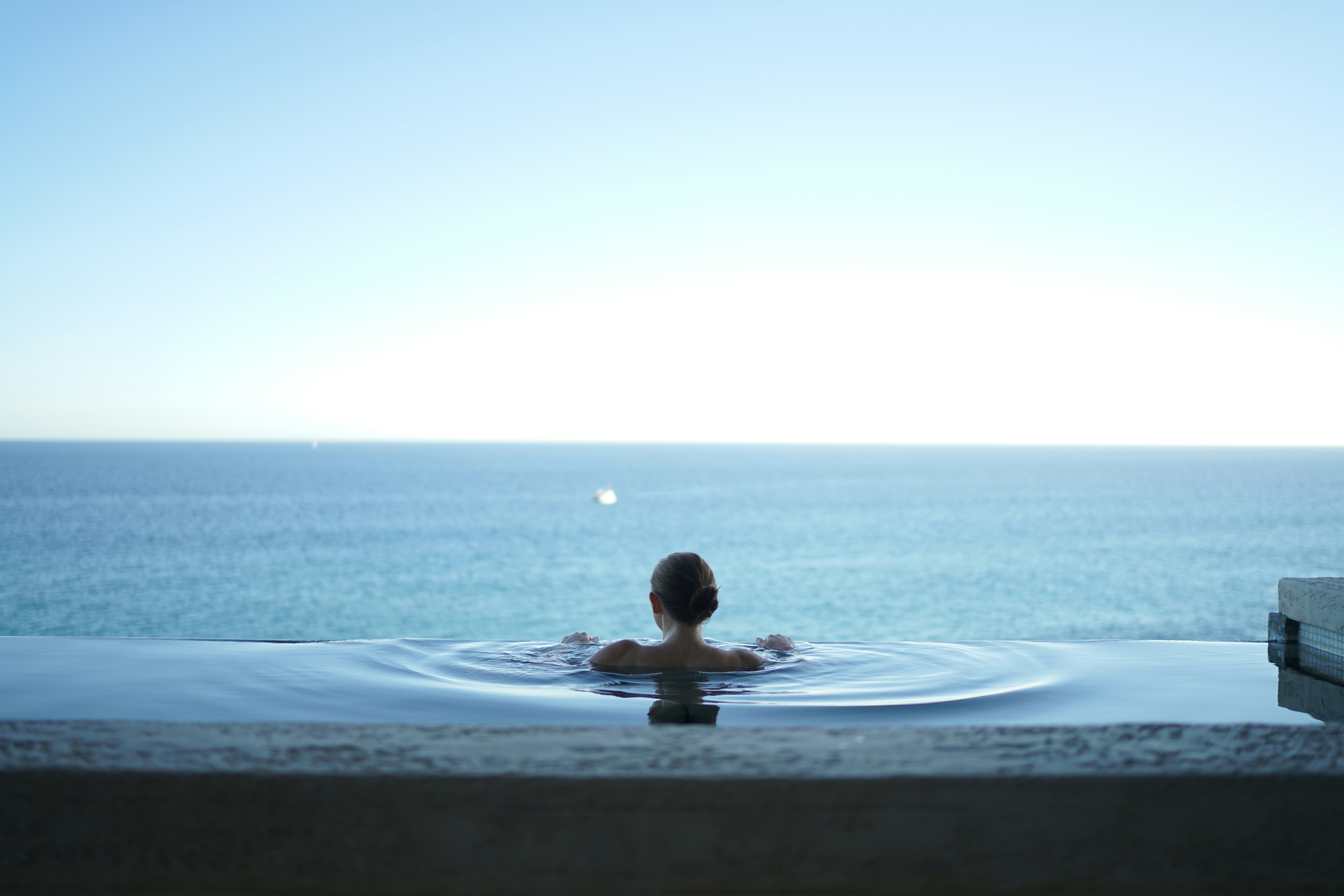 Person in infinity pool, looking at ocean.